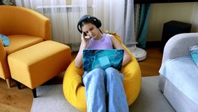 Young girl works on laptop in cozy living room while listening to music and relaxing in a bean bag chair - Powered by Shutterstock - Get 15% off with code: PIKWIZARD15