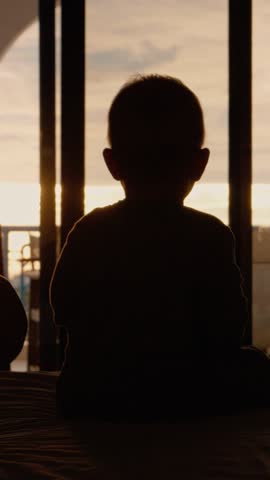 Vertical Screen: Silhouetted young mother the baby next to the window in bedroom. Silhouetted Young Girl Hugs Her Mother Next Window in Bedroom.