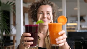 Healthy lifestyle concept featuring a woman presenting two glasses of colorful smoothies, one made of beetroot and the other of carrot, inside a modern restaurant - Powered by Shutterstock - Get 15% off with code: PIKWIZARD15