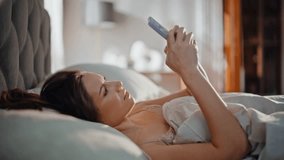 Awakened woman taking mobile phone receiving message early morning closeup. Sleepy beautiful brunette reading smartphone lying in cozy bed. Smiling lady texting cellphone napping in home bedroom. - Powered by Shutterstock - Get 15% off with code: PIKWIZARD15