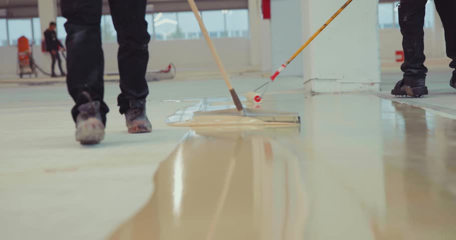 Construction workers spreading epoxy resin on a concrete floor using a notched trowel