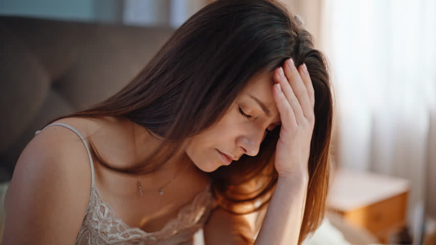 Sleepy woman suffering headache waking up in cozy home bed closeup. Unhappy lady feeling head pain after early wakeup in apartment bedroom. Sad young brunette experiencing health problem at morning.