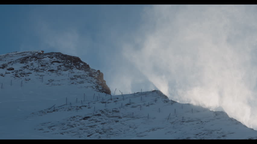 Strong wind blows snow off a rugged alpine peak, creating a dramatic blizzard-like effect in the Austrian mountains. Harsh light and mountain textures highlight the extreme winter conditions.