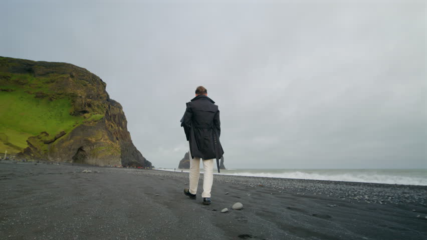 Back view of Young stylish man walking along at breathtaking Reynisfjara black sand beach in Iceland, captivated by the stunning cliffs and crashing waves, unforgettable memories of his adventure