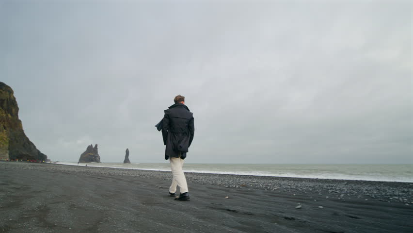 Back view of Young stylish man walking along at breathtaking Reynisfjara black sand beach in Iceland, captivated by the stunning cliffs and crashing waves, unforgettable memories of his adventure