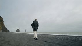 Back view of Young stylish man walking along at breathtaking Reynisfjara black sand beach in Iceland, captivated by the stunning cliffs and crashing waves, unforgettable memories of his adventure - Powered by Shutterstock - Get 15% off with code: PIKWIZARD15