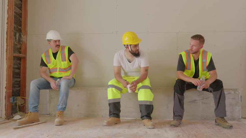 Diverse group of builders, including African American, Hispanic, and Caucasian individuals, on a break, talking at house renovations site, drinking water and resting