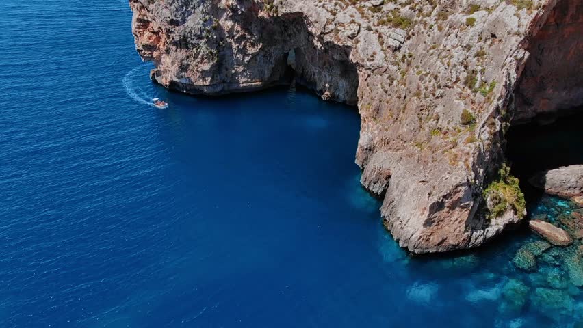 Aerial top view Blue Grotto in Malta. Pleasure boat with tourists runs. Natural arch window in rock.