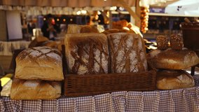 A variety of freshly baked loaves of bread are neatly arranged on a display table at a market. The loaves are golden-brown with crisp crusts and sit in a basket with a checkered cloth. Lights hang - Powered by Shutterstock - Get 15% off with code: PIKWIZARD15
