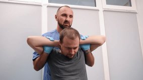 Chiropractic neck care, Patient therapy, Spinal adjustment. Wearing blue scrubs and gloves, chiropractor adjusts neck of male patient seated with his hands behind his head. - Powered by Shutterstock - Get 15% off with code: PIKWIZARD15