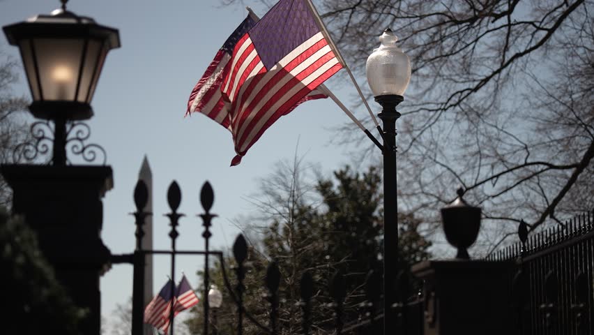 US flags on a post outside the presidents White House in Washington, DC with Washington Monument in distance.