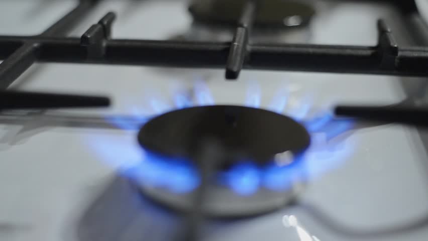 Blue flames bursting out of a gas stove. The flames are blue and very bright. Household gas stove, low light.