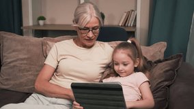 Grandmother and granddaughter share smiles as they solve interactive puzzles on a tablet during a cozy evening at home. Solving puzzles on a tablet - Powered by Shutterstock - Get 15% off with code: PIKWIZARD15