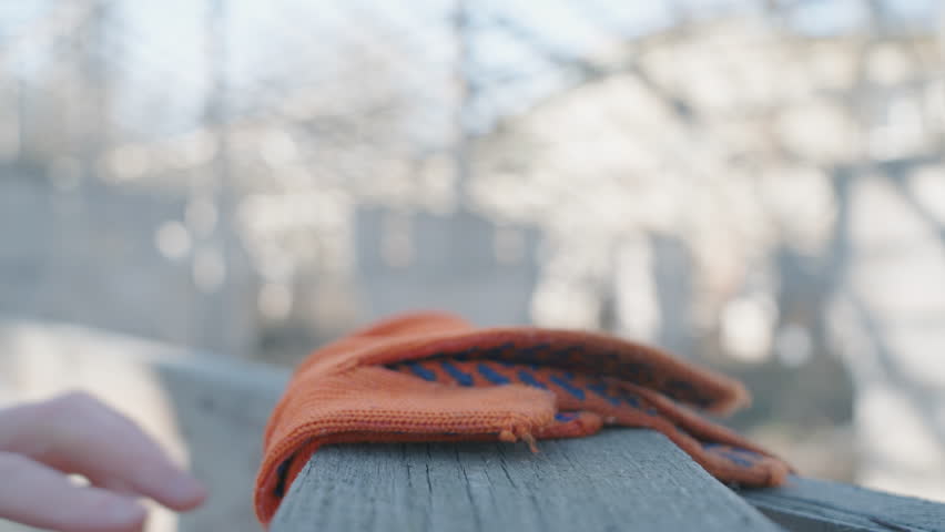 Construction Worker Placing Orange Work Gloves on Wooden Surface, Close-up View of Hand Putting Down Safety Gloves in Slow Motion with Blurred Background