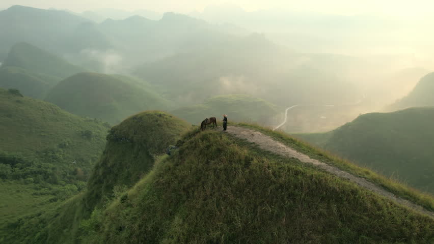 Aerial view of Ba Guang grass hill, Mountain range with fog and villager bringing horse to graze on the mountain in the morning at Ha Lang, Cao Bang, Vietnam
