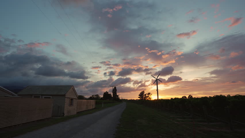 Beautiful vibrant sunrise over vineyard with wind turbine and cottage in countryside at New Zealand