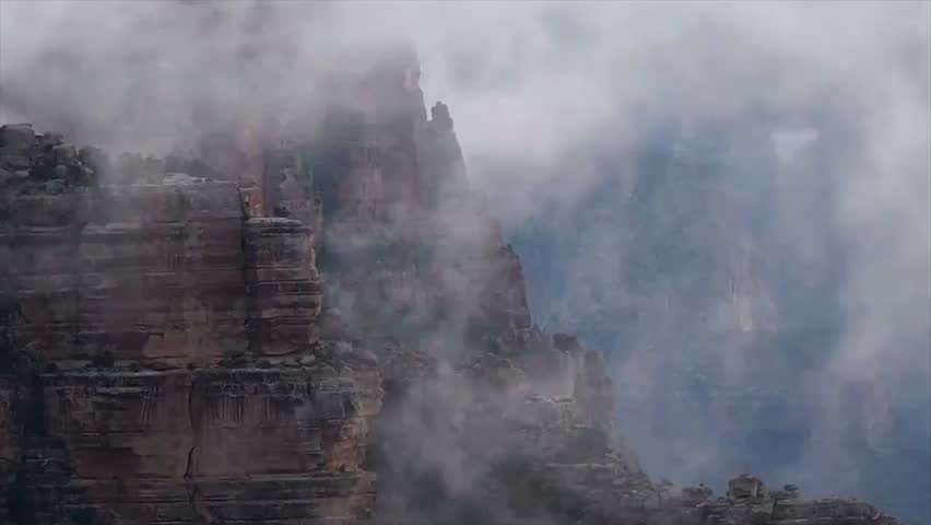 Mystical timelapse of thick fog and clouds moving through the Grand Canyon, partially revealing majestic layered cliffs. Moody, atmospheric view of this iconic natural wonder.
