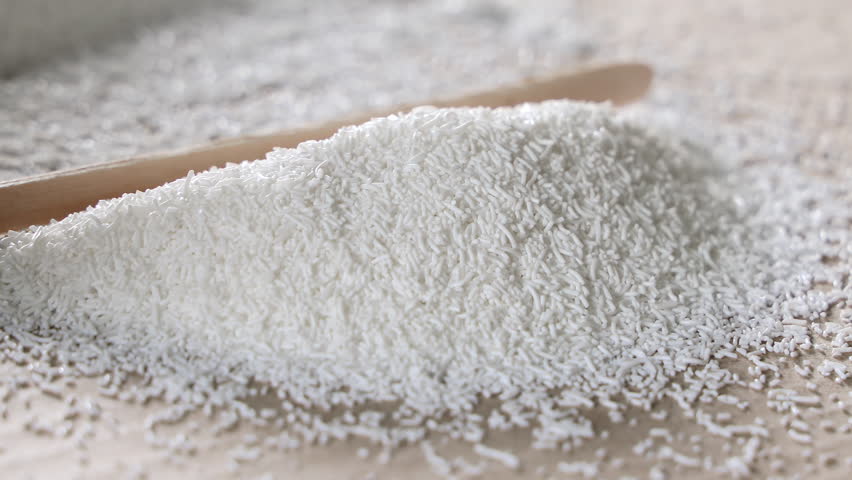 White plastic polymer granules spread and leveled with a wooden stick on cardboard, Close-up of raw material handling for plastic production or injection molding