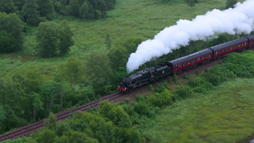 A steam train is traveling down the tracks. The train is black and red. The smoke coming from the train is white