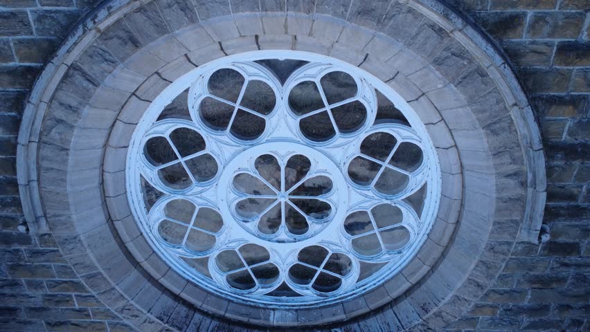 Close-up view of the large round stained-glass window in the center of the stone brick facade, topped with a gilded statue of St. Peter embedded between a pair of bell towers.  - Powered by Shutterstock - Get 15% off with code: PIKWIZARD15