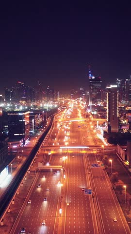 Top view of glowing night traffic weaving through highway interchanges surrounded by futuristic skyscrapers in the smart city of Dubai. Vibrant city lights, modern skyline, and urban architecture