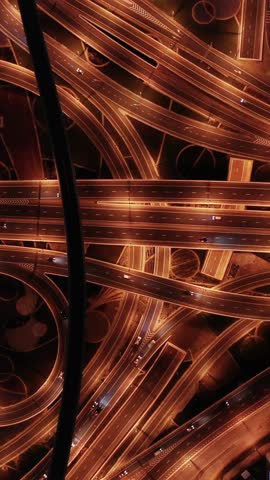 Top view of glowing night traffic weaving through highway interchanges surrounded by futuristic skyscrapers in the smart city of Dubai. Vibrant city lights, modern skyline, and urban architecture