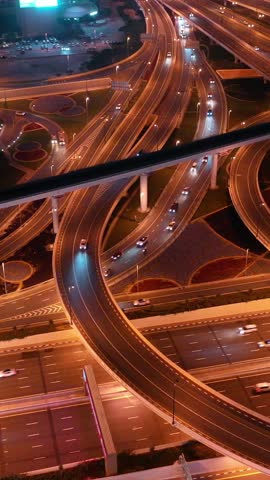 Top view of glowing night traffic weaving through highway interchanges surrounded by futuristic skyscrapers in the smart city of Dubai. Vibrant city lights, modern skyline, and urban architecture