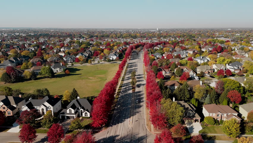 Beaut Scenic suburban street surrounded by vibrant red and yellow autumn trees. Warm fall colors create a picturesque seasonal neighborhoods, homes, aerial view.