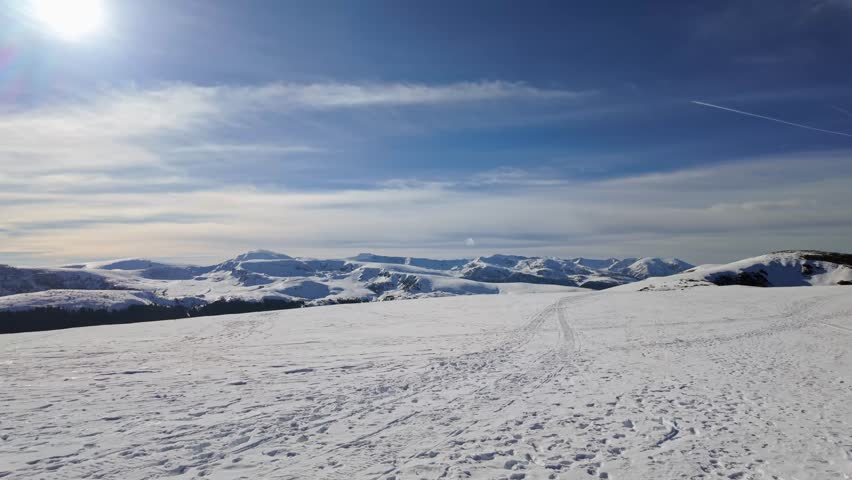 Magnificent winter view from the peak of the Transalpina ski resort, where snow-covered slopes meet the striking Urdele Hill and the towering Parang Mountains in Romania.