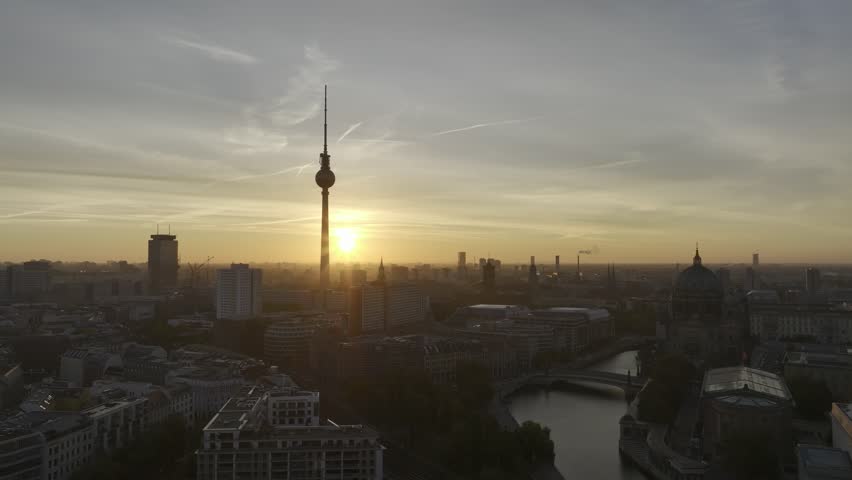 A drone view of Berline television tower at sunset highlighting the cityscape with the Spree River weaving through urban buildings in warm hues