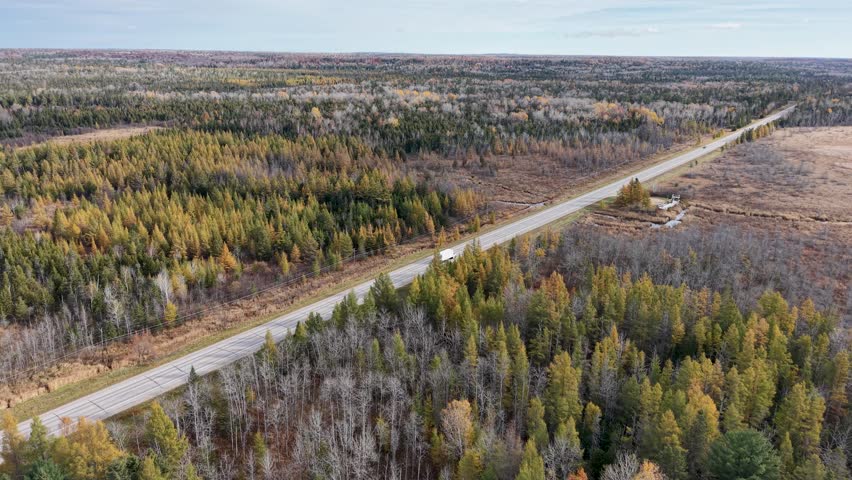 Drone footage flying above a remote highway cutting through a colorful autumn forest in Michigan’s Upper Peninsula