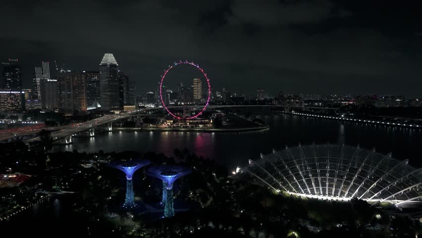 Fly over Supertree Grove and Flower Dome towards Singapore Flyer at night