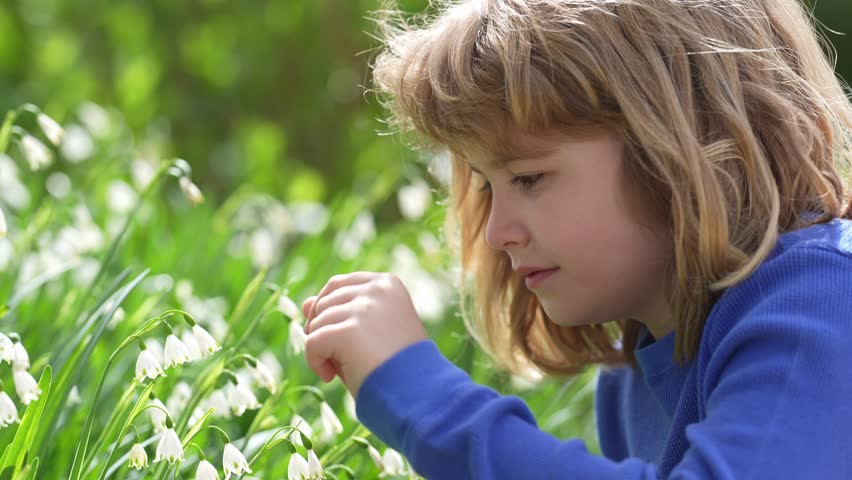 Tender kids Spring. Child smell snowdrop in spring garden. Kid dreaming face in summer snowflake. Kid play with snowdrop on spring day. Happy child during spring blossom. Beauty kids face.
