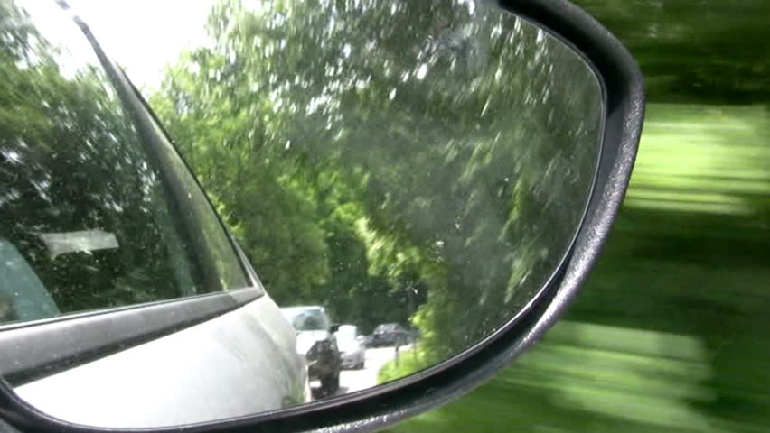 View to rear-view mirror of car. The car leaves from the forest on a mountain