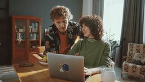 Young diverse couple looking together at laptop screen, smiling and talking at kitchen table in sunny living room. Zoom shot - Powered by Shutterstock - Get 15% off with code: PIKWIZARD15