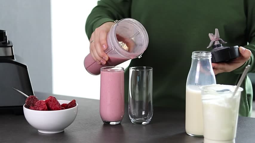 Close up of a woman in green sweater preparing fresh strawberries smoothie with yogurt and milk in the kitchen 