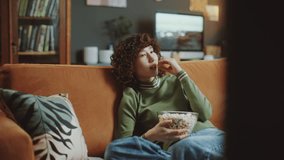 Young Asian woman with curly hair lounging on sofa, snacking on popcorn, watching television and smiling in cozy living room - Powered by Shutterstock - Get 15% off with code: PIKWIZARD15