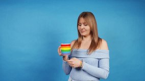 Studio shot of a young woman savoring a hot drink from a vibrant rainbow mug, isolated on a blue backdrop - Powered by Shutterstock - Get 15% off with code: PIKWIZARD15