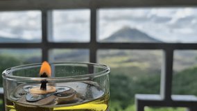 Close-up shot of a lit candle in a clear glass container, with the Gunung Abang mountain visible in the blurred background. The candle's flame flickers gently, creating a warm and intimate atmosphere. - Powered by Shutterstock - Get 15% off with code: PIKWIZARD15