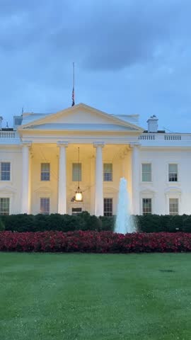 White House glowing at night with flag and trees. Vertical video