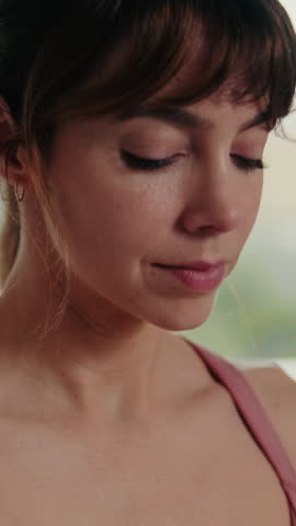 Vertical video, Young woman doing yoga and stretching exercises in her apartment. She is wearing comfortable clothes and concentrating on her movements.