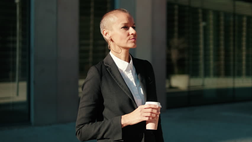 Businesswoman takes a coffee break outside her corporate building. She enjoys the moment, takes a sip and looks around.