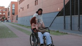 Happy multi ethnic friends are walking down the street, a young woman is pushing her red haired friend in a wheelchair, they are chatting and enjoying the walk - Powered by Shutterstock - Get 15% off with code: PIKWIZARD15