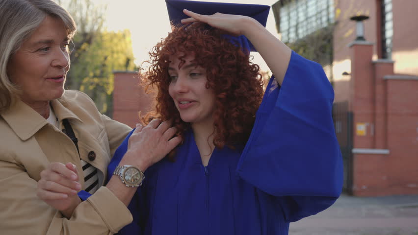 Proud mother gently adjusting graduation cap, sharing emotional moment of academic milestone and familial connection during daughter