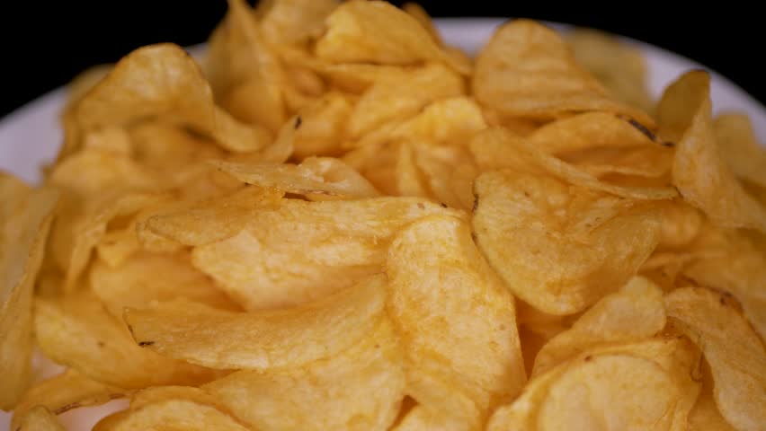Potato chips spinning on white plate. Guy takes potato chips with his hand. Close-up.