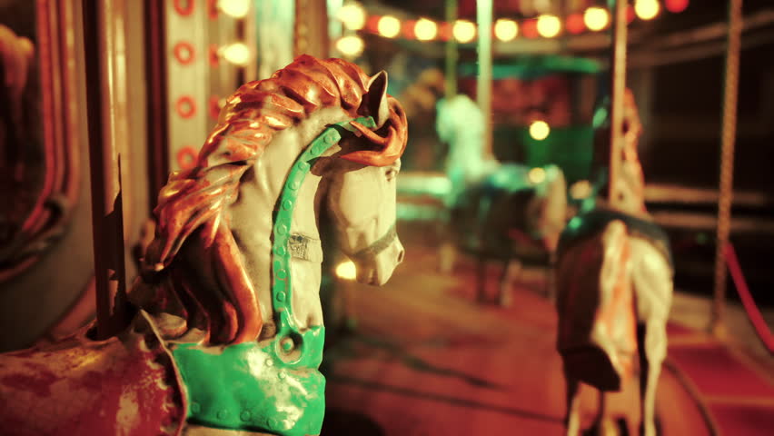 The amusement park lies silent under the night sky, illuminated by colorful lights. A deserted carousel spins slowly, showcasing intricately detailed horses, evoking a sense of nostalgia.