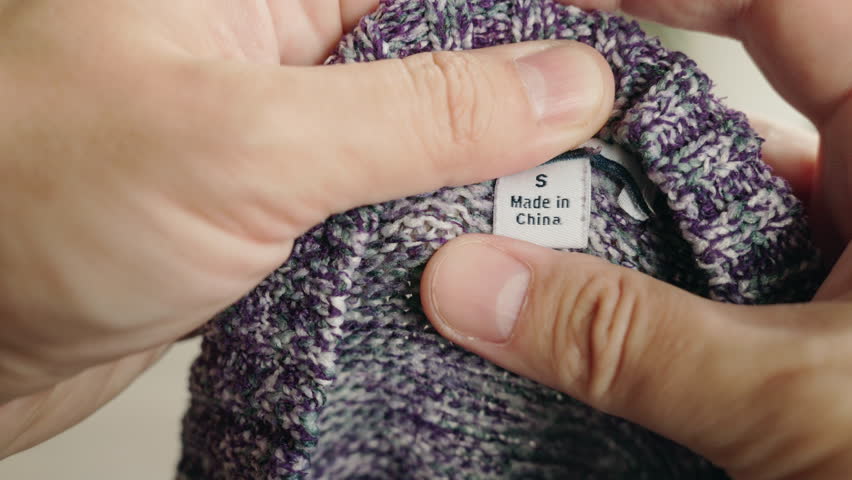 Close-up of hands holding a black clothing label marked "Made in China" 