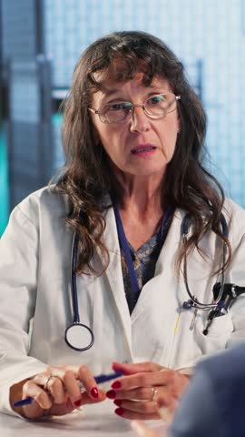 Vertical Video Senior doctor and patient discussing diagnostic results in a modern medical office, showcasing advanced technology using records files displaying x rays and MRI scans. Care management