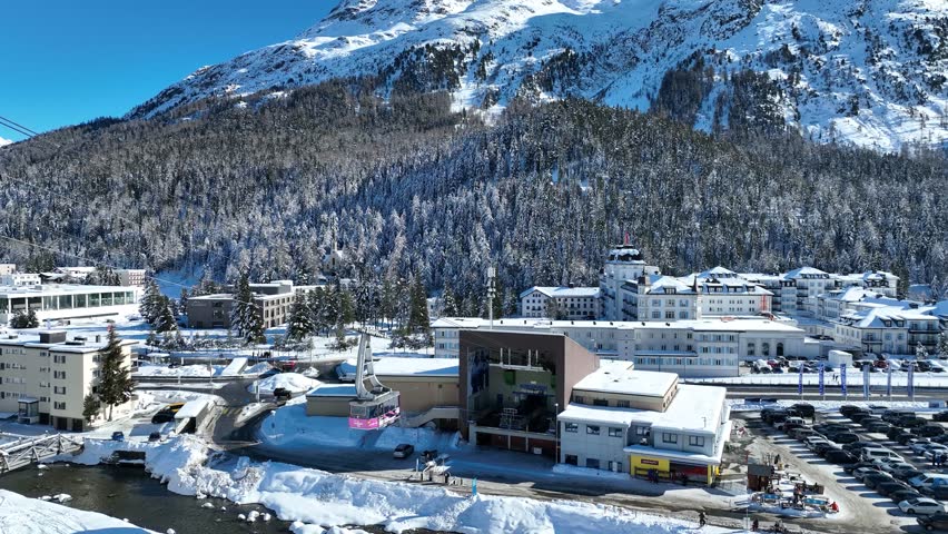 ST. MORITZ, SWITREZLAND, FEBRUARY 4, 2025: Pink cable car gondola lift arrives to St. Moritz Bad station. Cabin of ski-lift in the Engadin ski resort with mountain in the distance