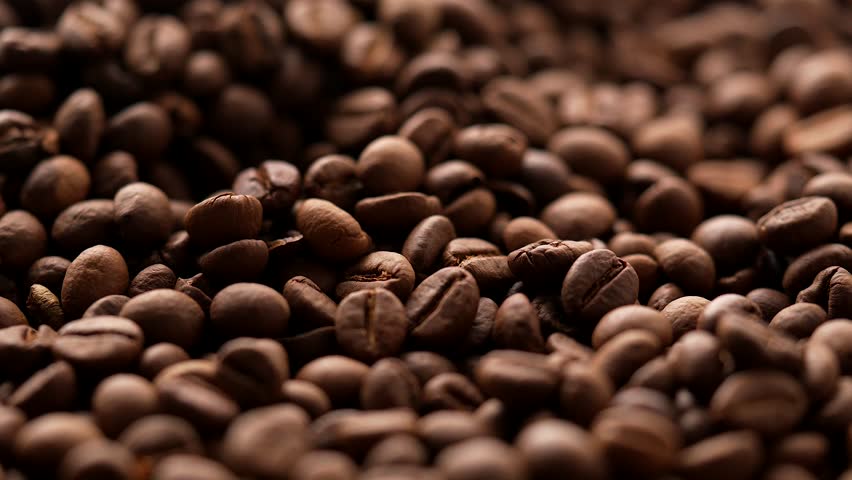 A closeup shot of a heap of roasted coffee beans rotating under bright natural light, with blurred background